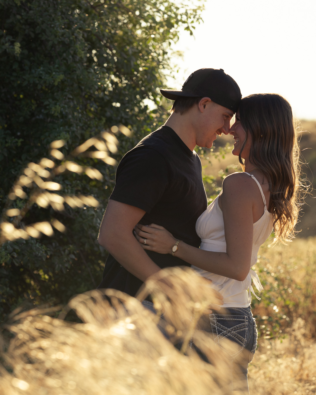 Couple touching foreheads and smiling in a sunlit field at golden hour